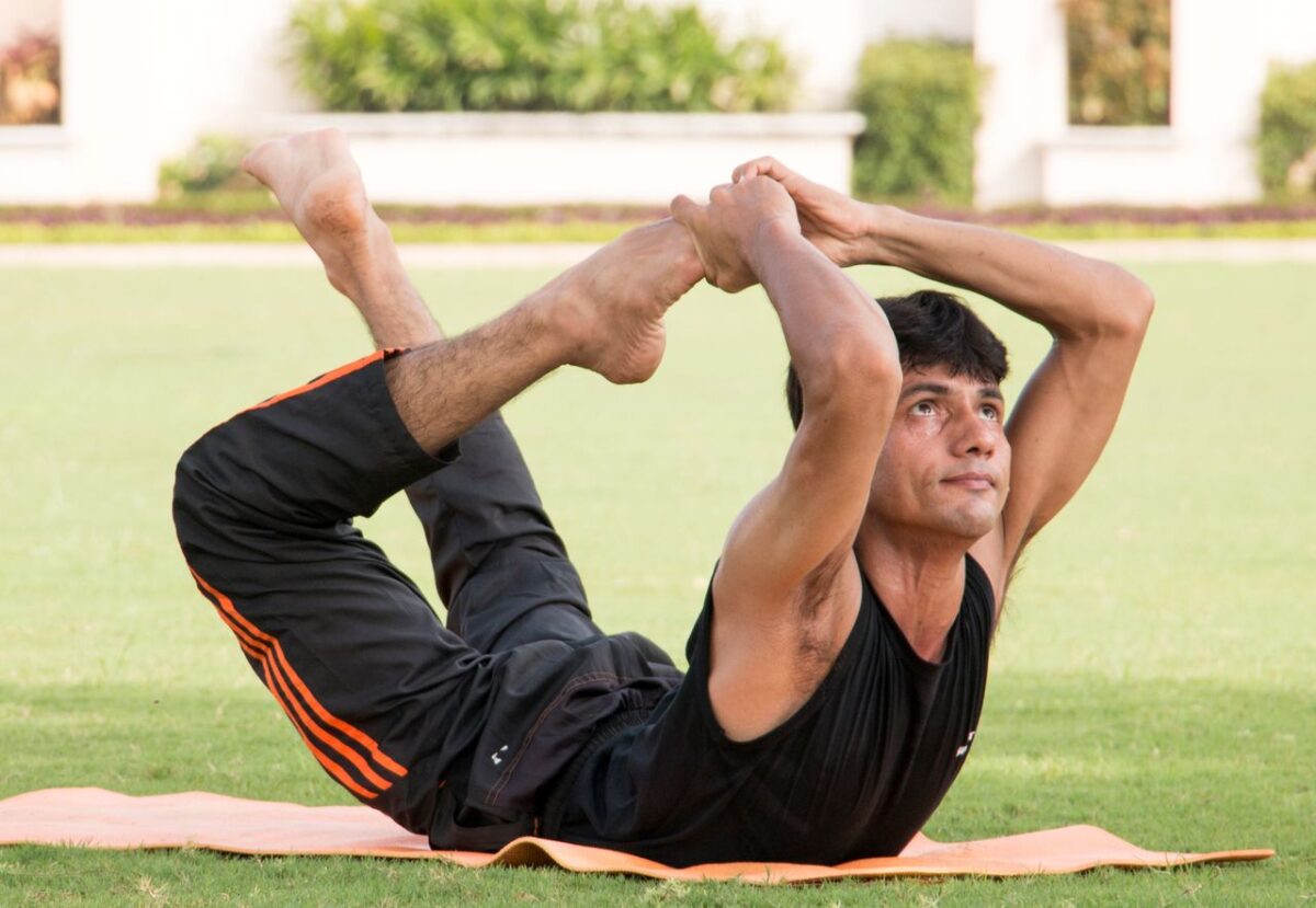 CREPS CRJS Centre Adult man demonstrating a yoga pose on a grass mat outdoors, showcasing flexibility and fitness.