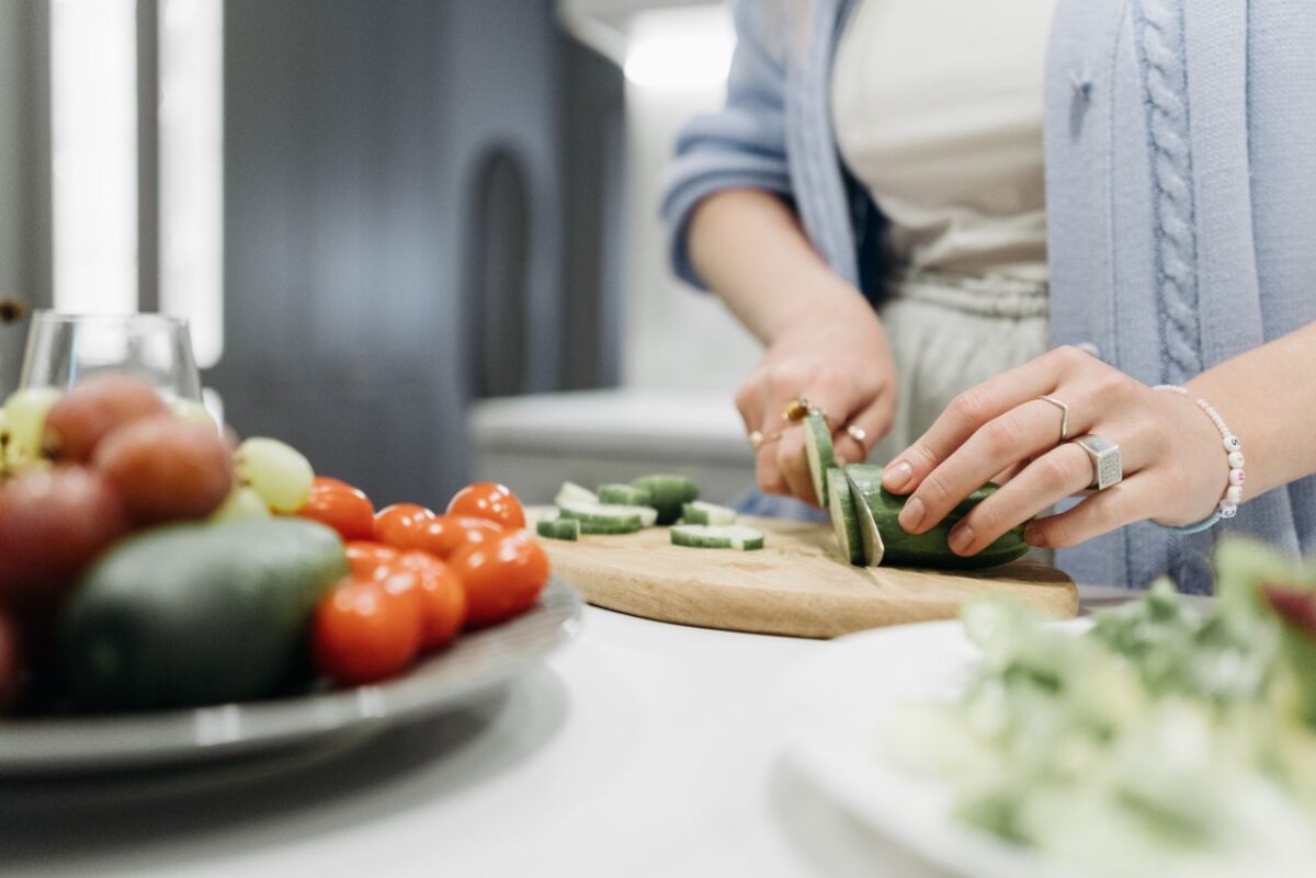 CREPS CRJS Centre Close-up of a woman slicing cucumbers on a wooden board surrounded by fresh vegetables.